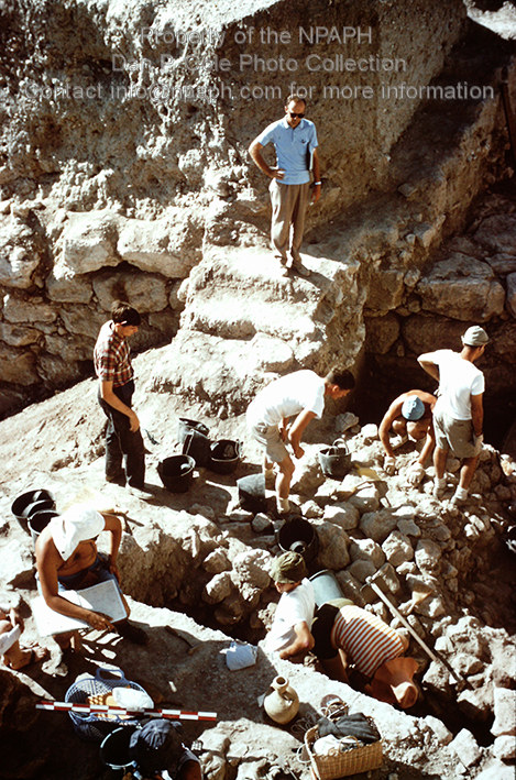 Field I; Our digging “fields” usually consisted of 4 areas. The supervisor of this area is standing at left, while one of the crew of six is entering information. (1967, ID: cColepGezer057, Source: slide, Repository: NPAPH-project Creator(s): Dan P. Cole)