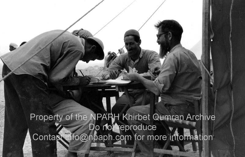 Pay-day. De Vaux is sitting in front of a tent paying a local worker. Presumably the recipient is signing for receipt (25 March 1954; ID: cBoerpQumran12.22; Source: photo; Depository: NPAPH; Creator(s): Leo Boer)